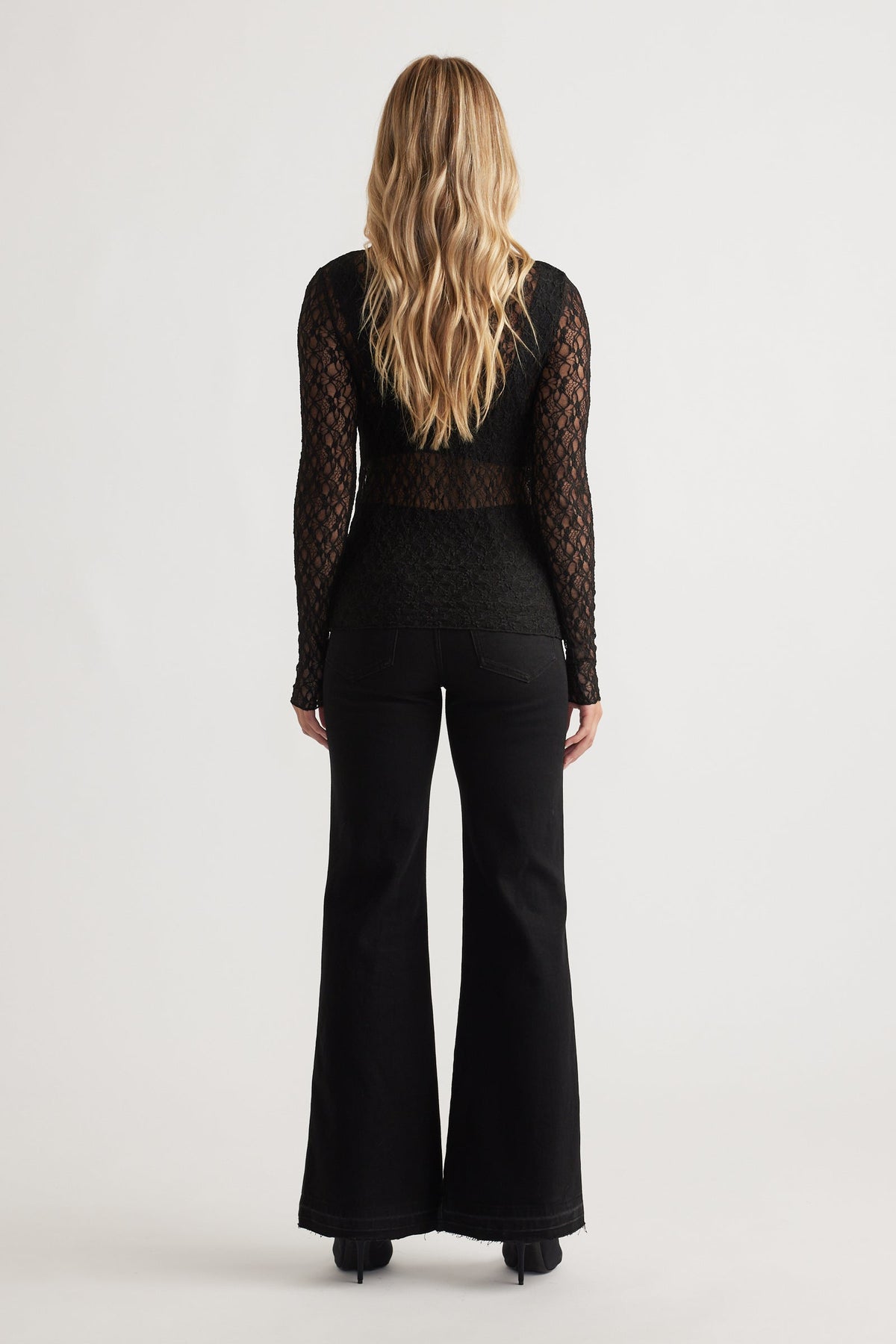 Woman wearing a fitted black lace long sleeve top with sheer detailing paired with high-waisted black flared jeans