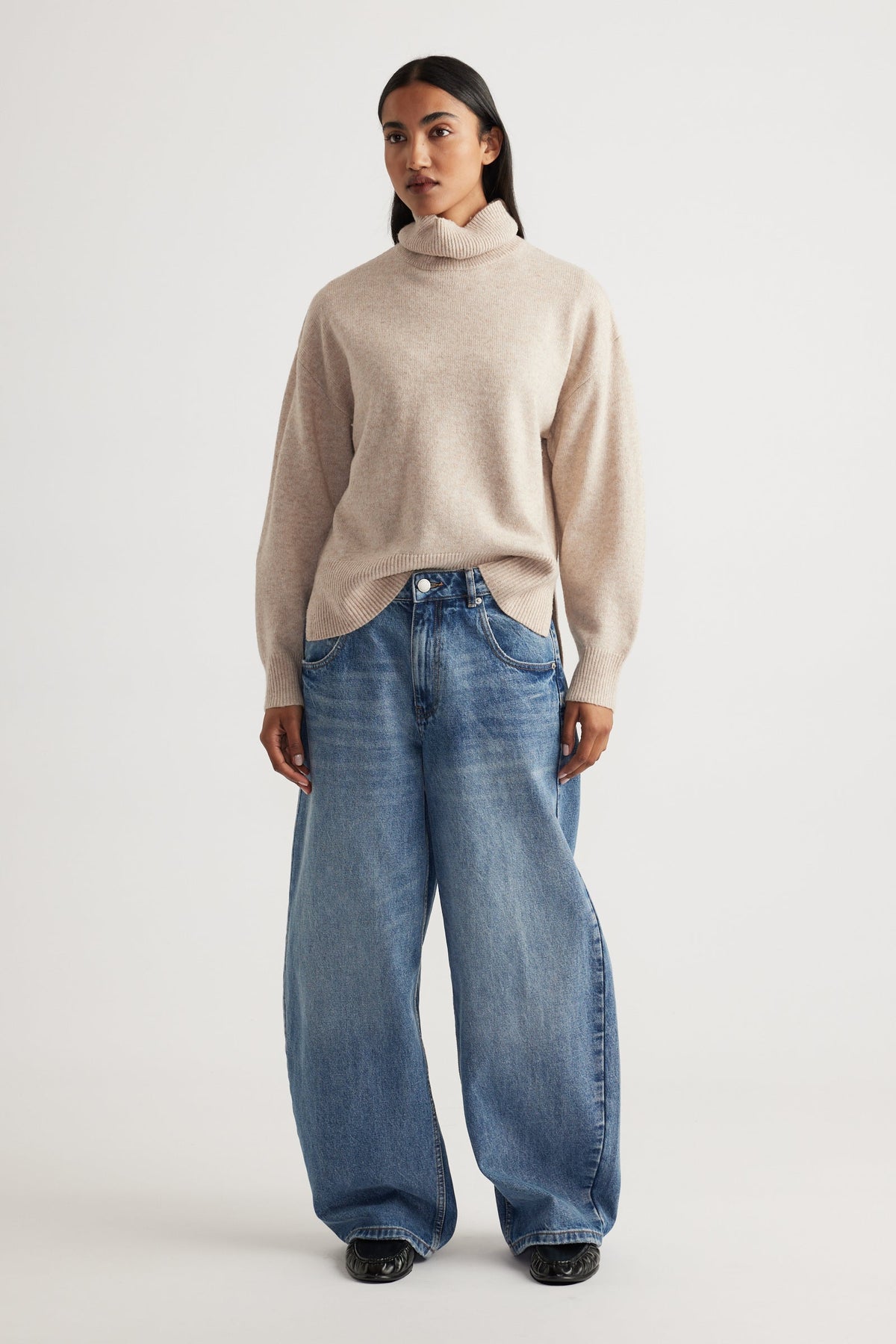 Woman modeling Roll Neck Knit Jumper in soft beige knitwear paired with relaxed wide-leg denim jeans by Decjuba Australian brand