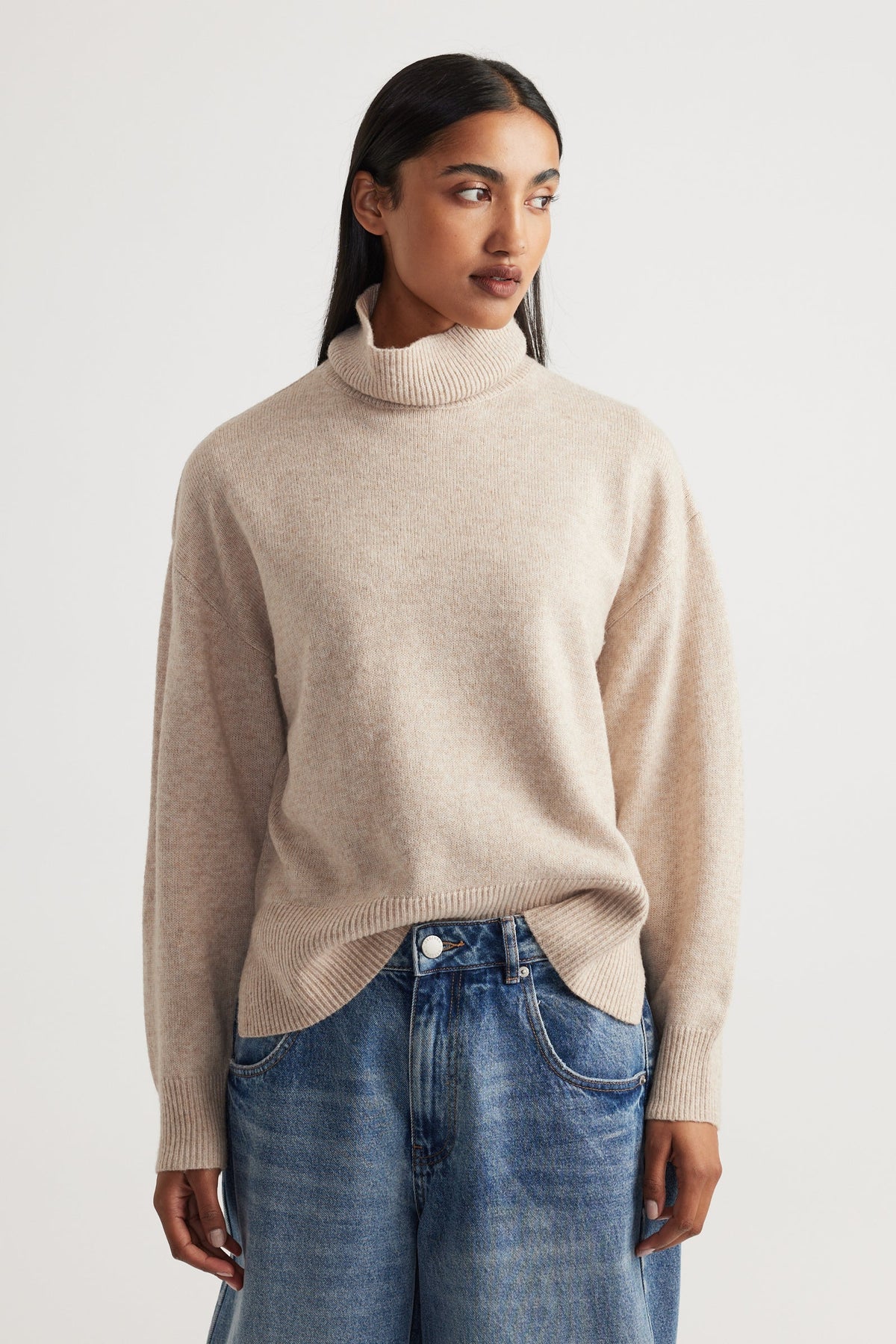 Woman wearing Roll Neck Knit Jumper in soft beige knitwear styled with relaxed blue denim jeans by Decjuba Australian brand