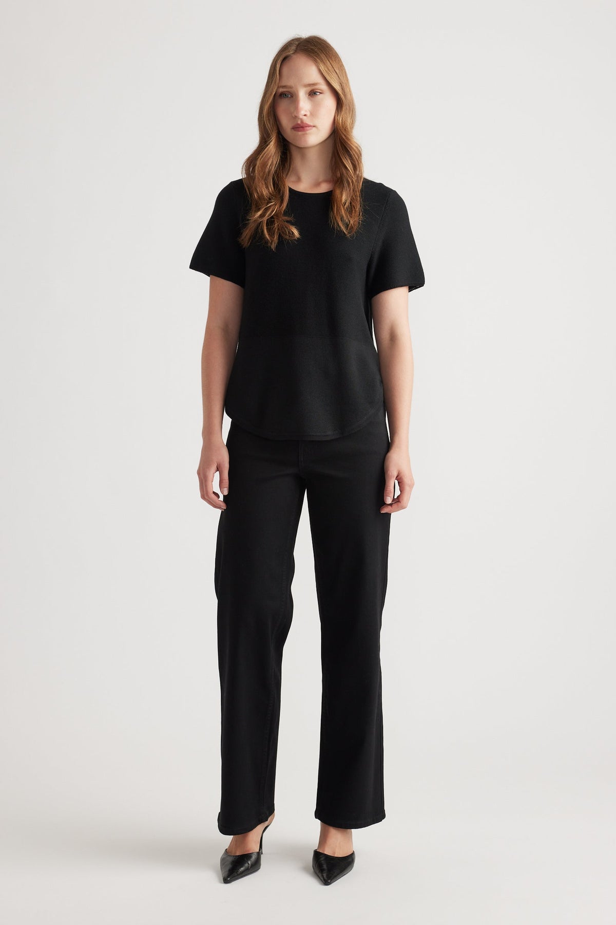 Woman wearing a black knitted short sleeve top paired with straight leg black pants and black pointed heels