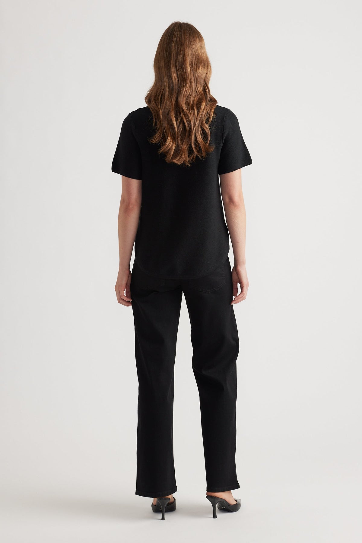 Woman wearing a relaxed black knitted short sleeve top paired with straight black pants and black heels from the back view