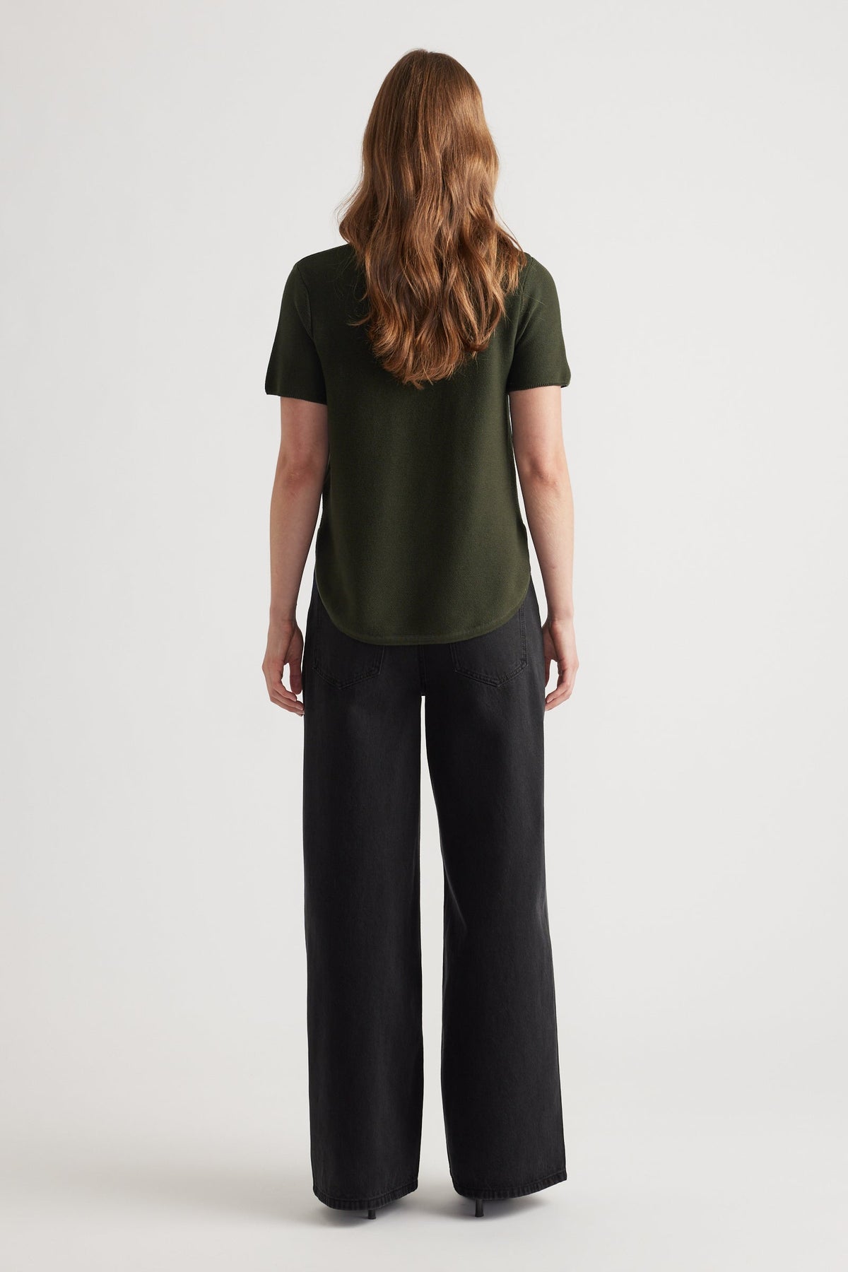 Woman seen from behind wearing a forest green short sleeve knit top paired with wide-leg black pants
