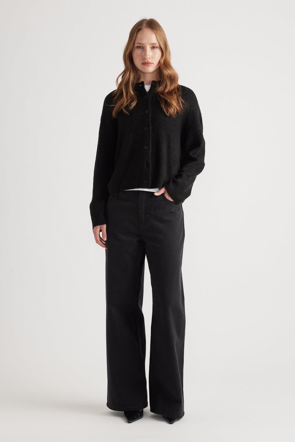 Woman wearing a relaxed black knit cardigan paired with wide-leg black denim jeans for a minimalist look