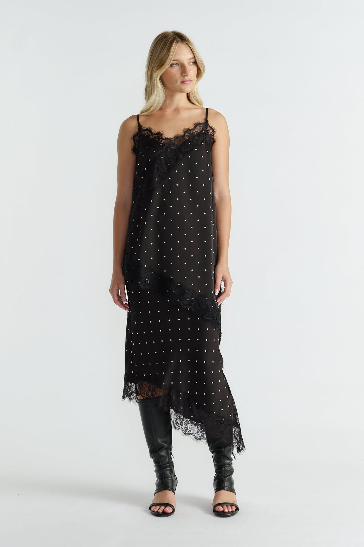 Woman wearing a black lace-trimmed tunic with thin straps and polka dot print paired with knee-high black boots