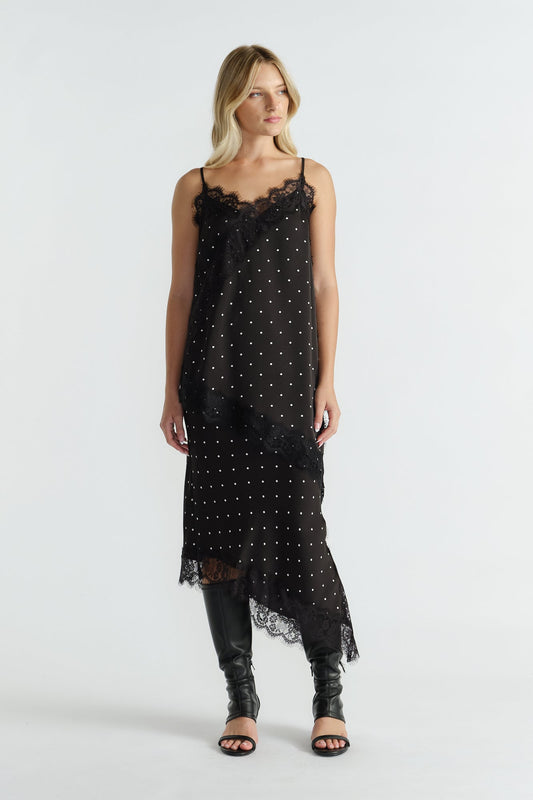 Woman wearing a black lace-trimmed tunic with thin straps and polka dot print paired with knee-high black boots