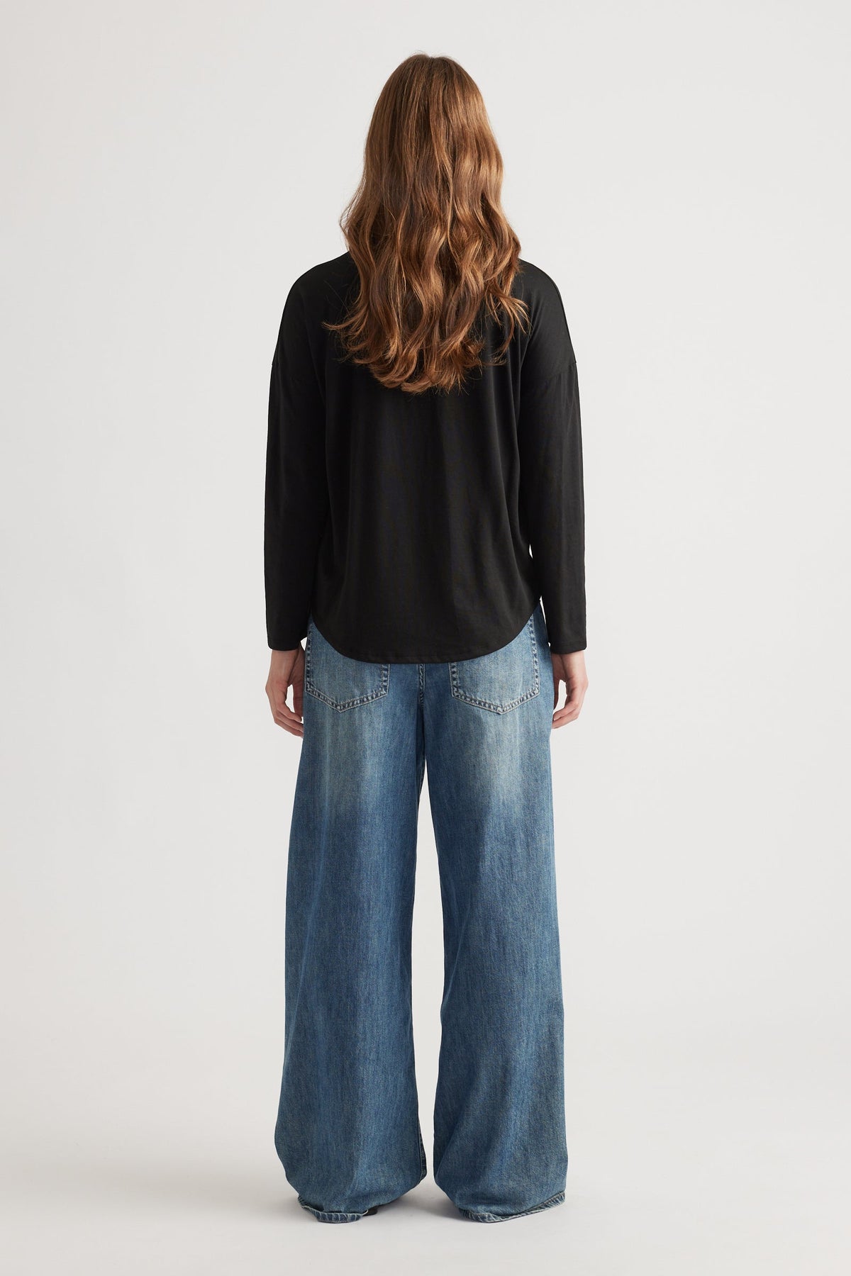 Woman wearing a relaxed black long sleeve top paired with wide-leg faded blue denim jeans for a casual look