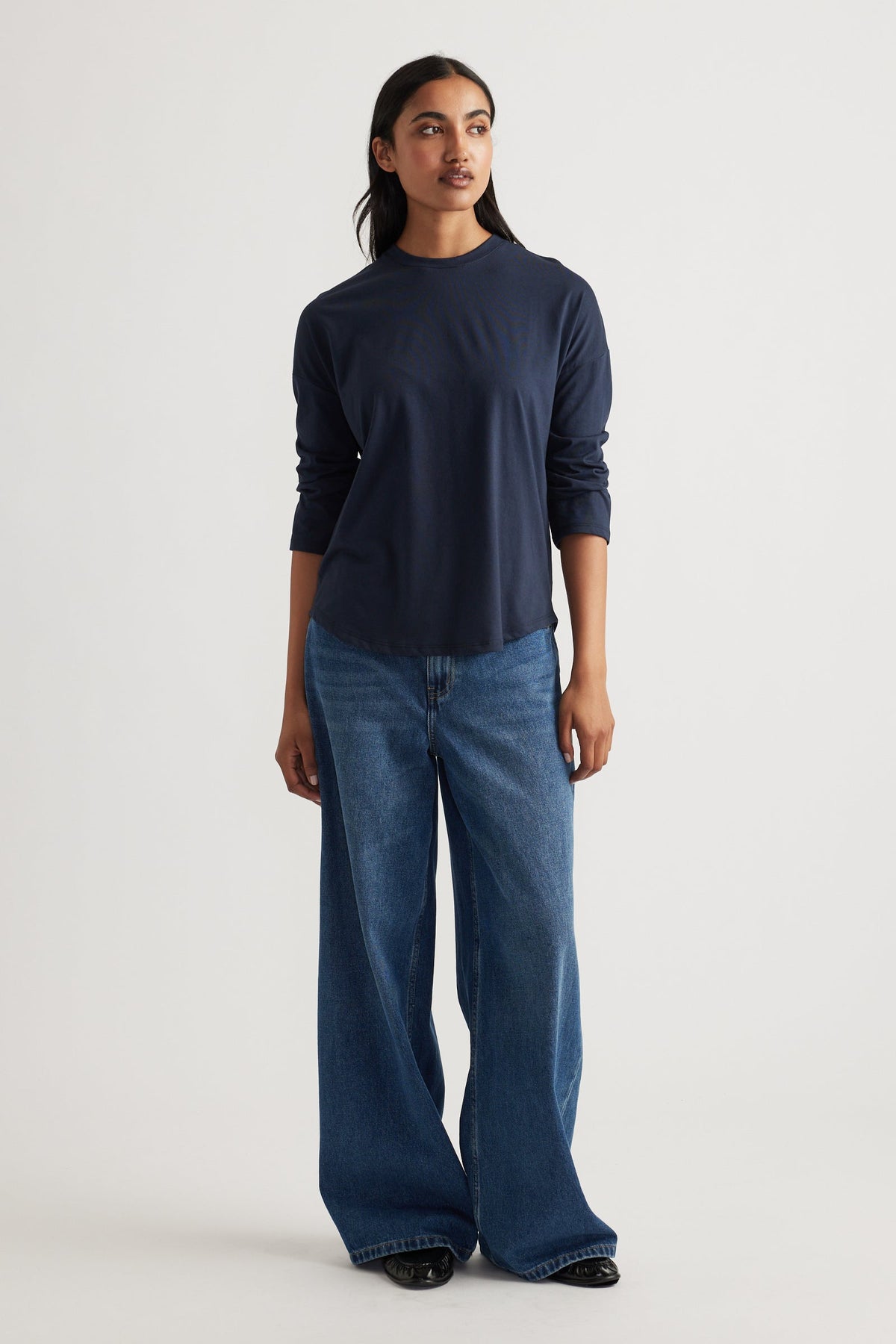 Woman wearing a navy long sleeve top paired with relaxed wide-leg classic blue denim jeans and black shoes