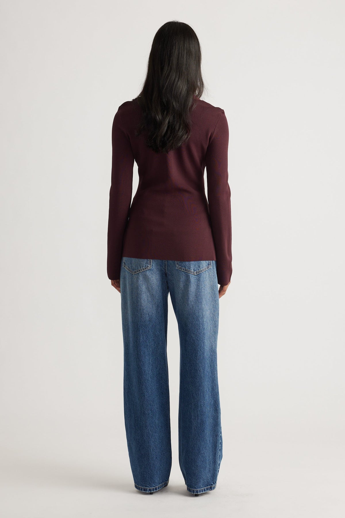 Woman seen from behind wearing a fitted long-sleeve burgundy knit top paired with relaxed wide-leg blue denim jeans