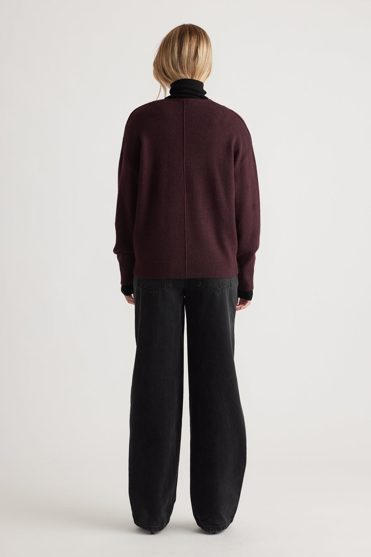 Back view of a deep burgundy knit sweater with subtle seam detail paired with loose-fitting black pants