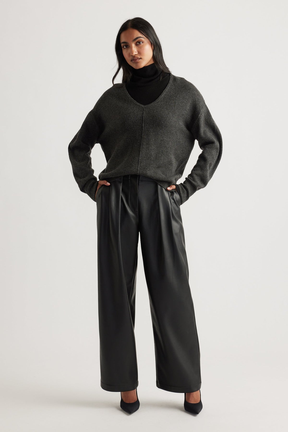 Woman wearing a charcoal knit jumper with a deep V-neck and seam detail, paired with black wide-leg trousers and heels