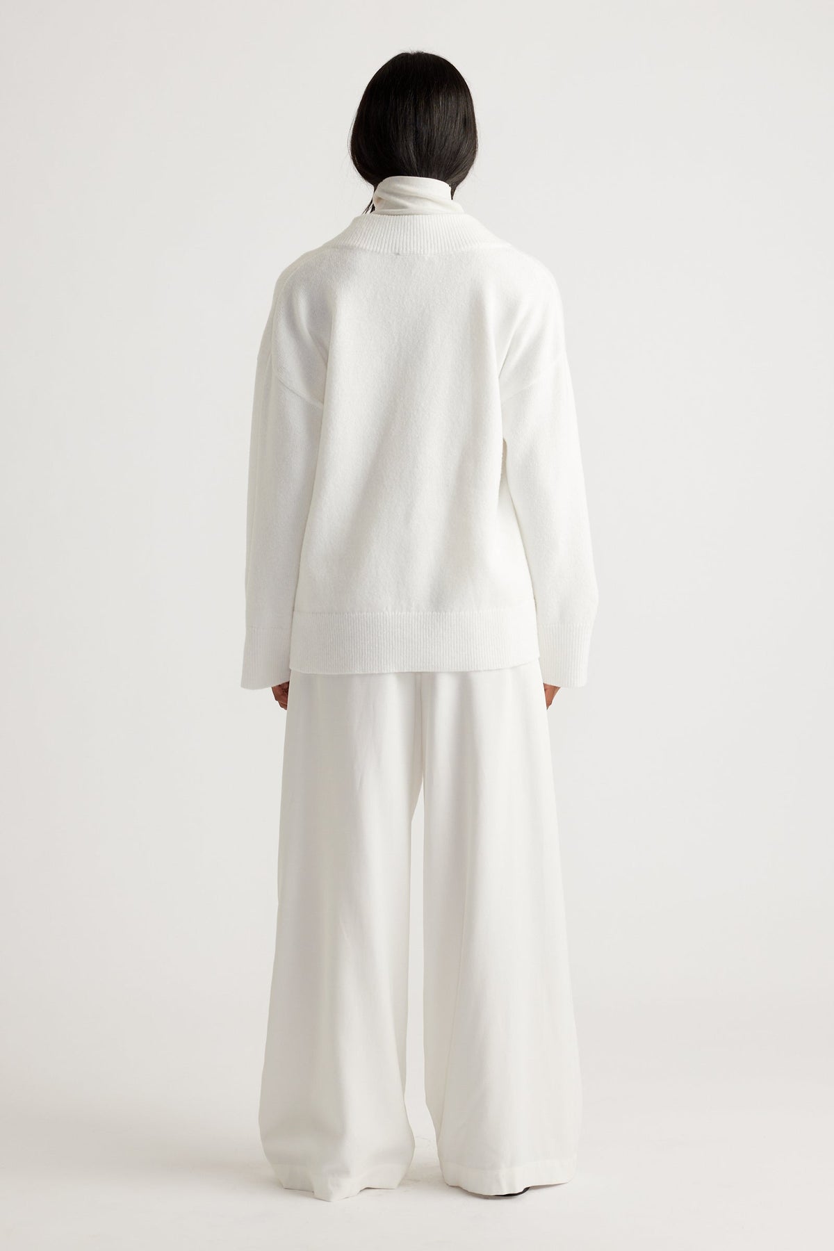 Woman wearing an oversized white knit sweater paired with wide-leg trousers for a relaxed, minimalist look