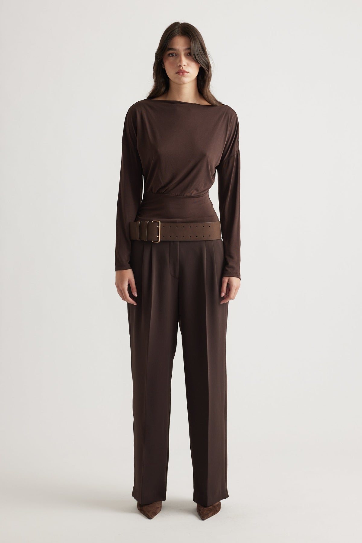 Woman wearing a fitted brown cinched long sleeve top with wide belt, paired with matching tailored trousers for a sleek look