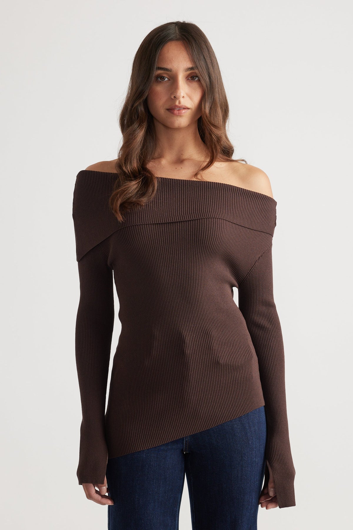 Fitted rich mocha ribbed knit top with asymmetrical off-shoulder neckline paired with dark blue jeans