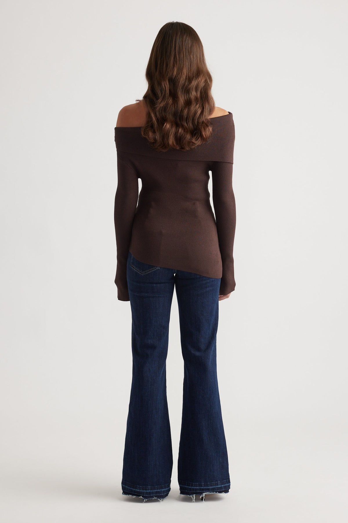 Woman wearing a rich mocha off-shoulder knit top paired with dark flared denim jeans and loose waves hair