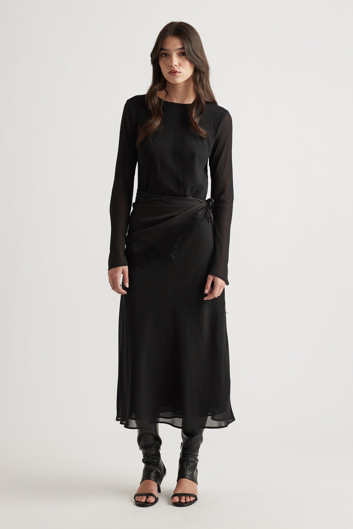 Elegant black maxi dress with sheer long sleeves and a delicate wrap detail, styled with black heeled sandals.