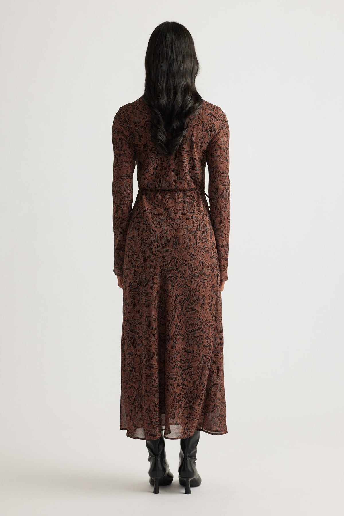 Woman wearing a fitted brown patterned maxi dress with long sleeves, paired with black heeled boots for a sleek look