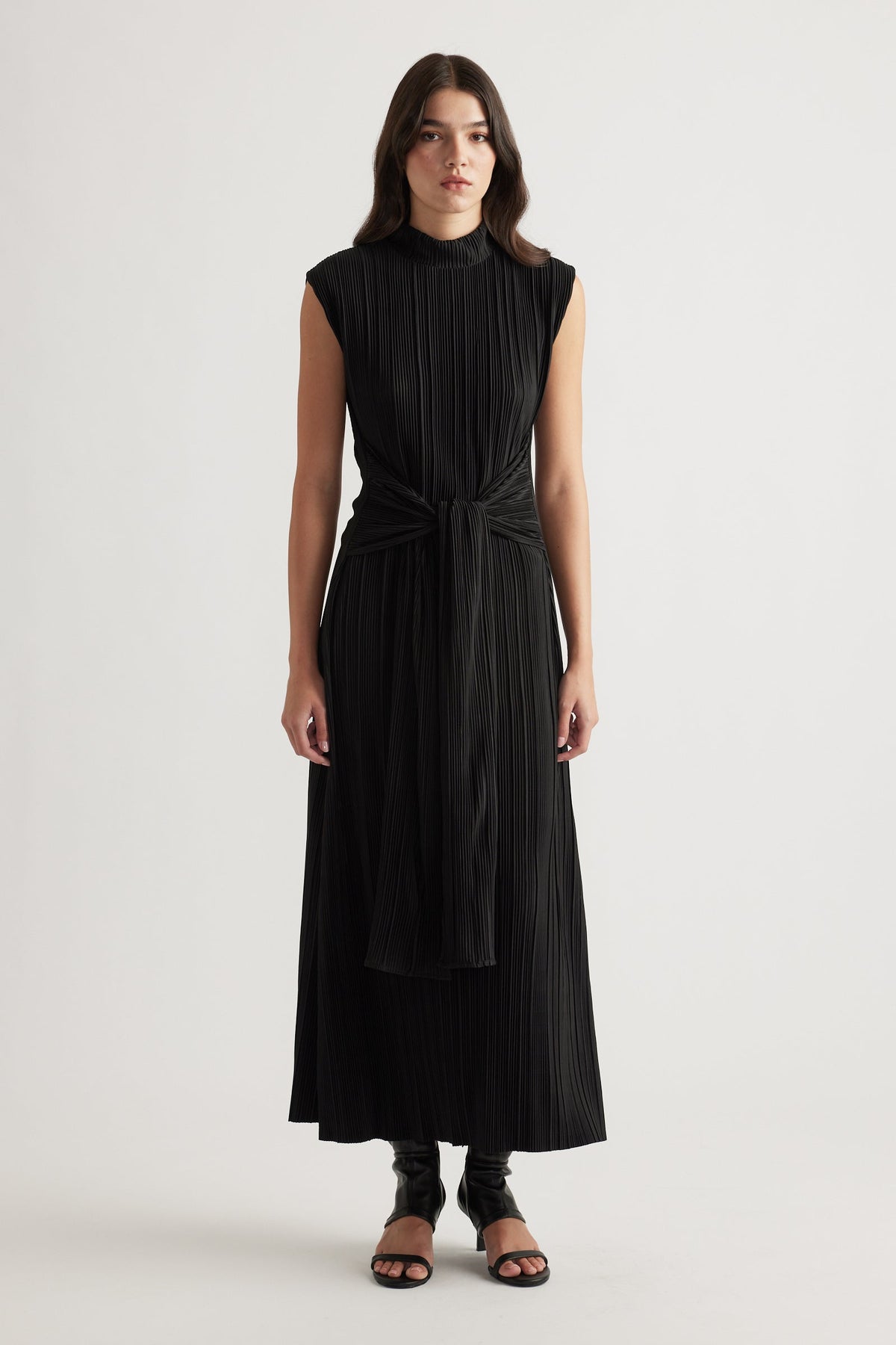 Sleeveless black maxi dress with pleated texture and front tie detail, styled with open-toe heels for a sleek look