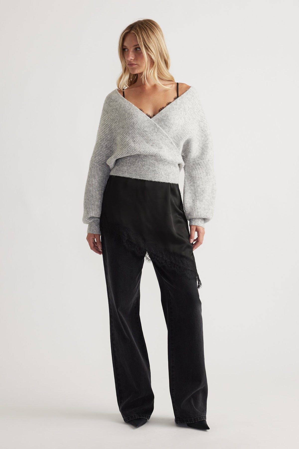 Woman wearing a light grey crossover knit jumper with voluminous sleeves paired with black satin wide-leg pants with lace trim