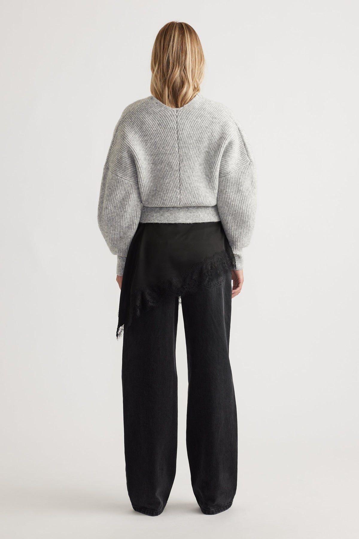 Woman seen from behind wearing a light grey knit jumper with balloon sleeves and wide-leg black pants with lace detail