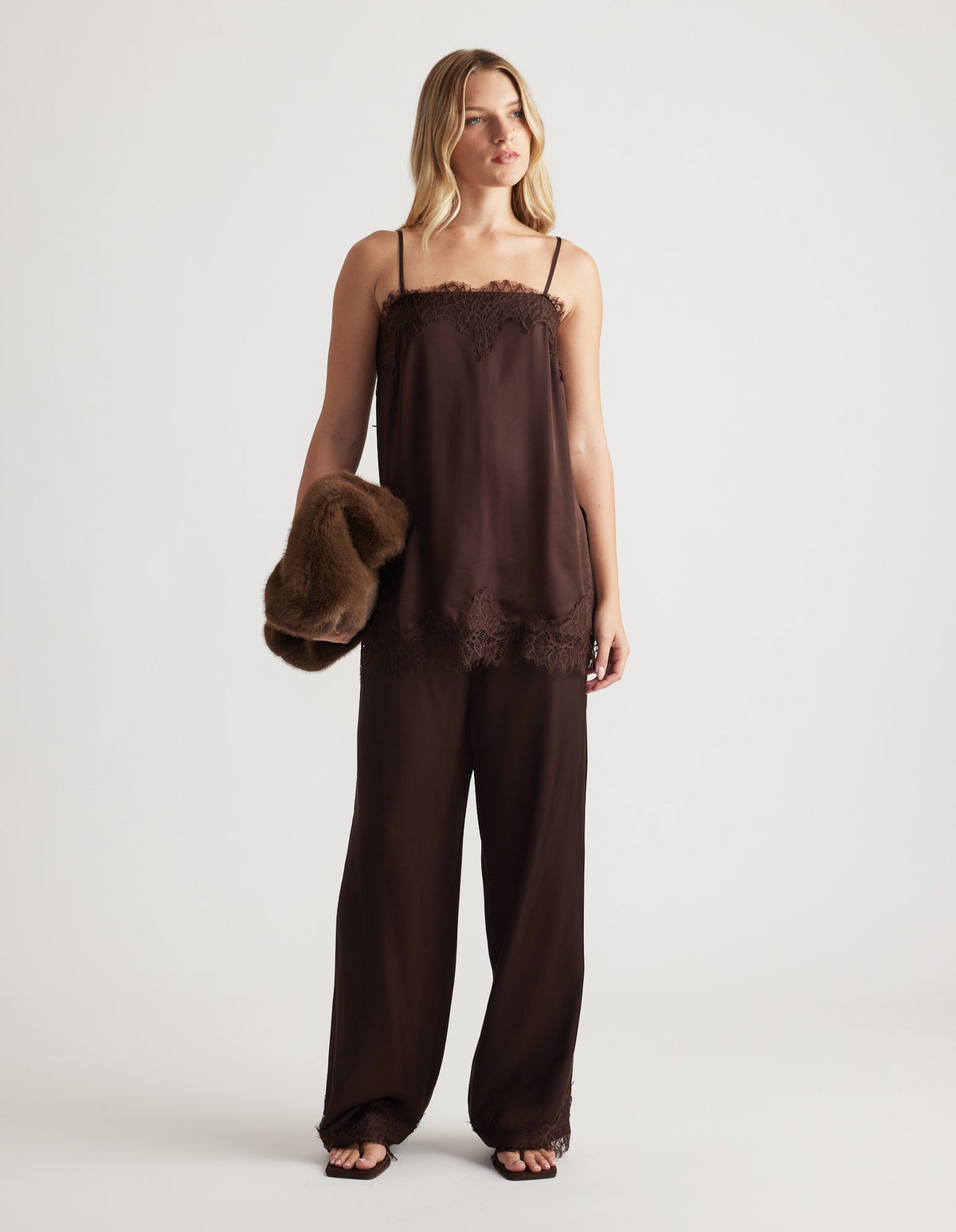 Woman wearing a rich mocha lace-trimmed cami top with matching wide-leg pants and holding a plush brown jacket