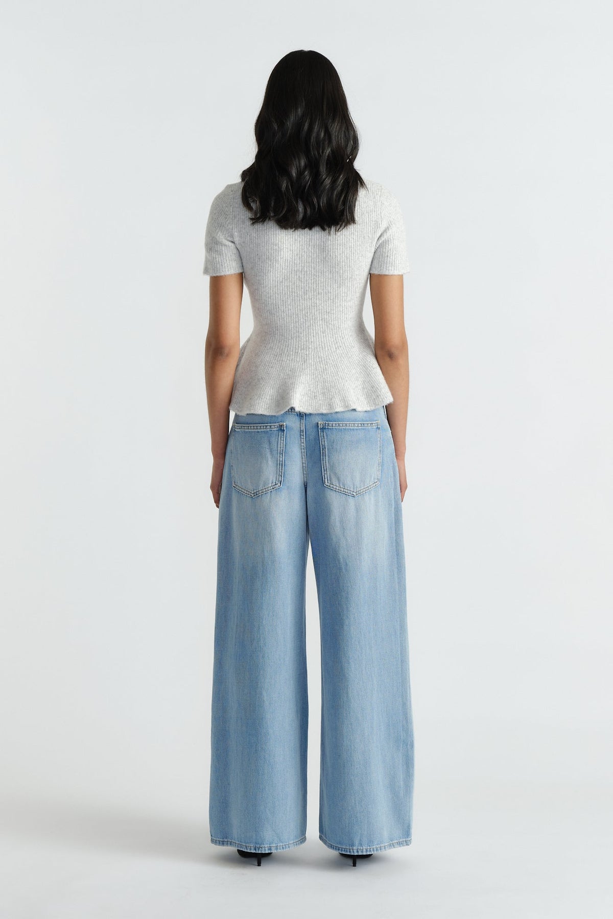 Woman wearing a light grey peplum knit top paired with wide-leg light blue denim jeans for a casual look