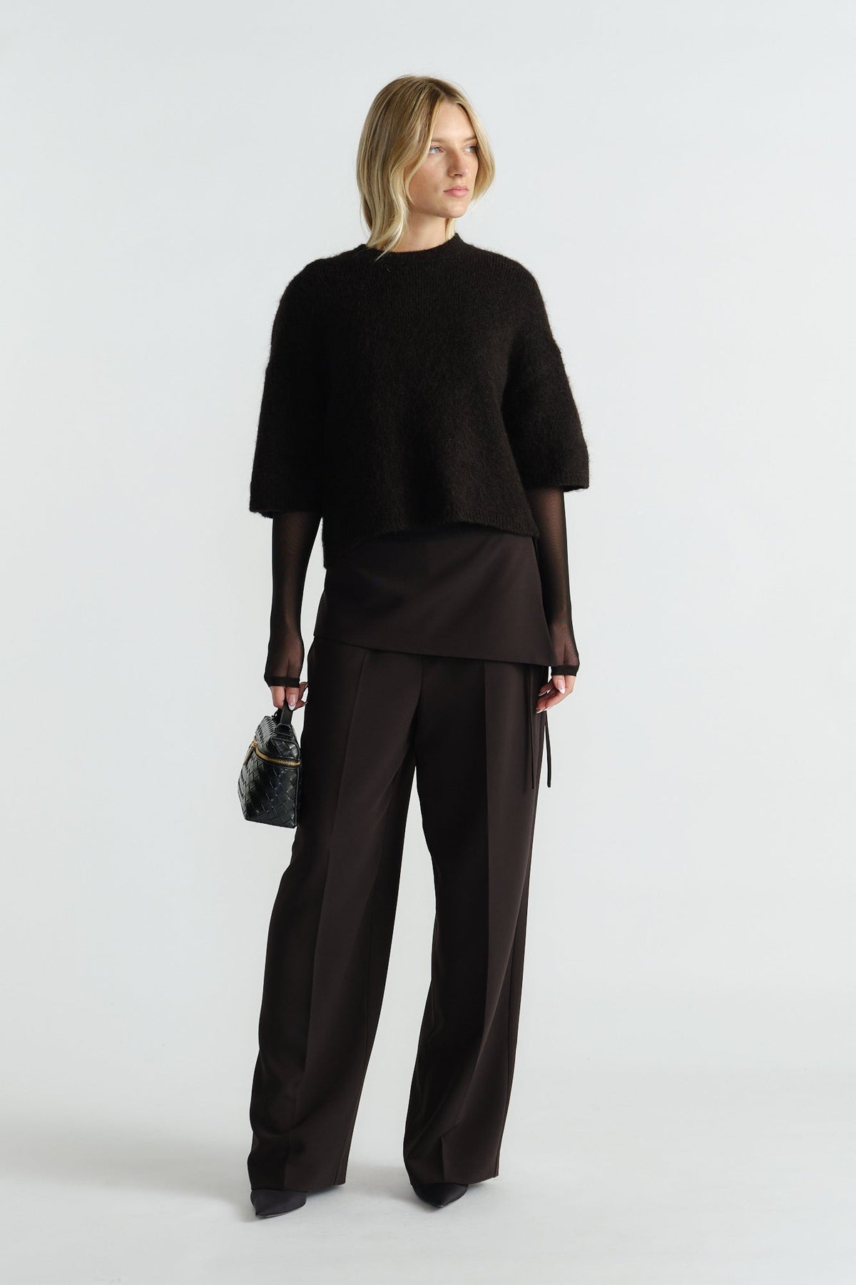 Woman wearing a black fluffy knit tee layered over a sheer long-sleeve top with wide-leg tailored black pants.