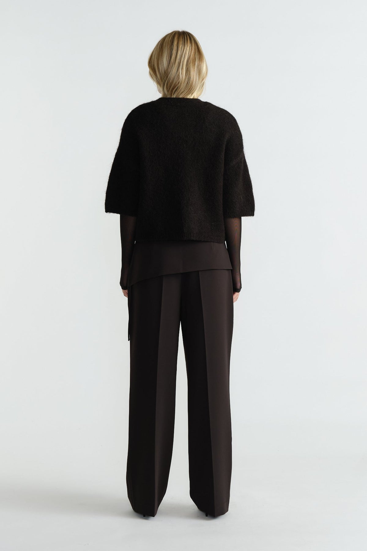 Woman wearing a black fluffy knit tee layered over a sheer long-sleeve top paired with wide-leg black pants, back view.