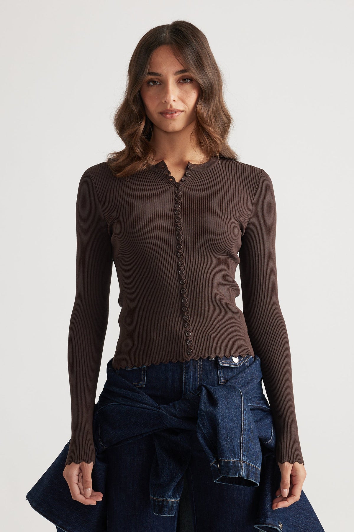 Fitted ribbed mocha top with delicate scalloped edges and button details paired with dark blue denim jeans and jacket tied at waist