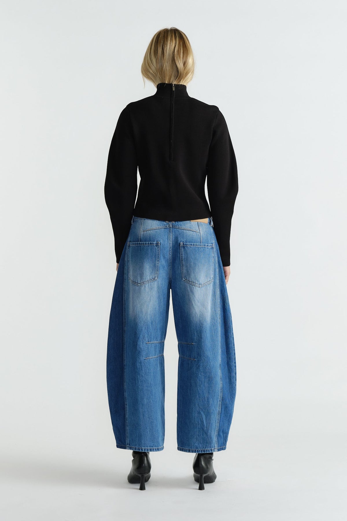 Back view of woman wearing a fitted black high neck jumper paired with wide-leg faded blue jeans and black ankle boots.