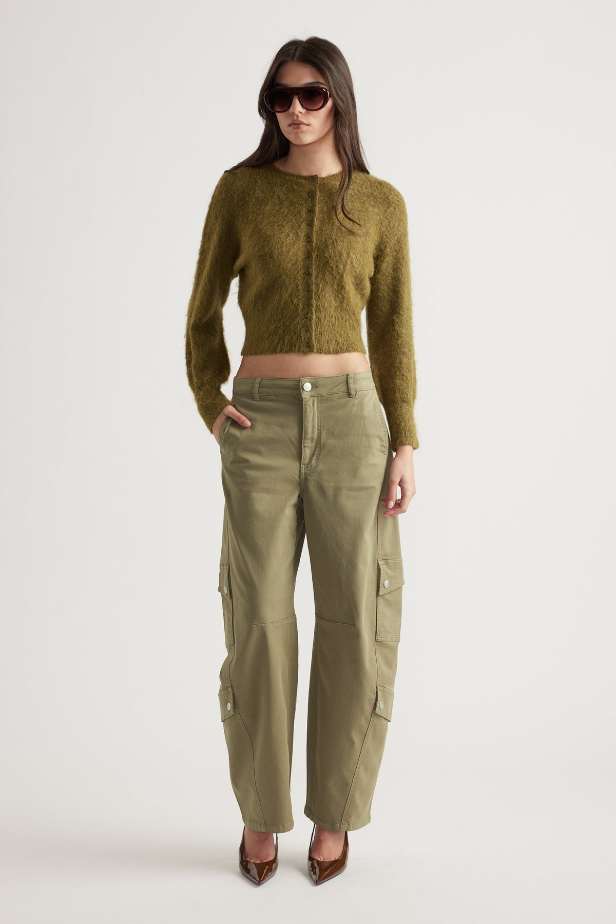 Woman wearing a cropped olive button-up cardigan paired with high-waisted cargo pants and brown pointed heels
