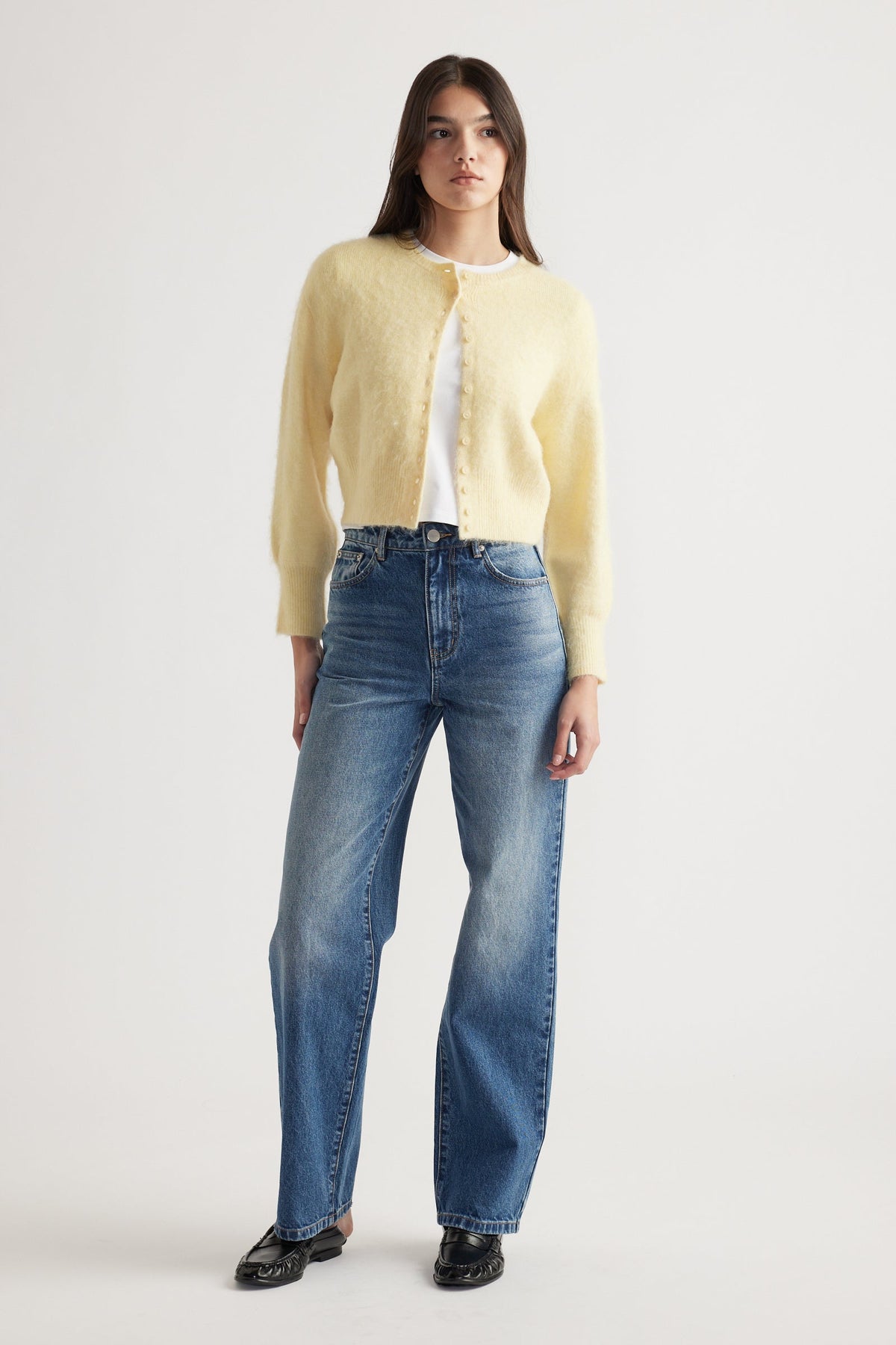 Woman wearing a soft lemon button-up cardigan paired with classic high-waisted blue denim jeans and black loafers
