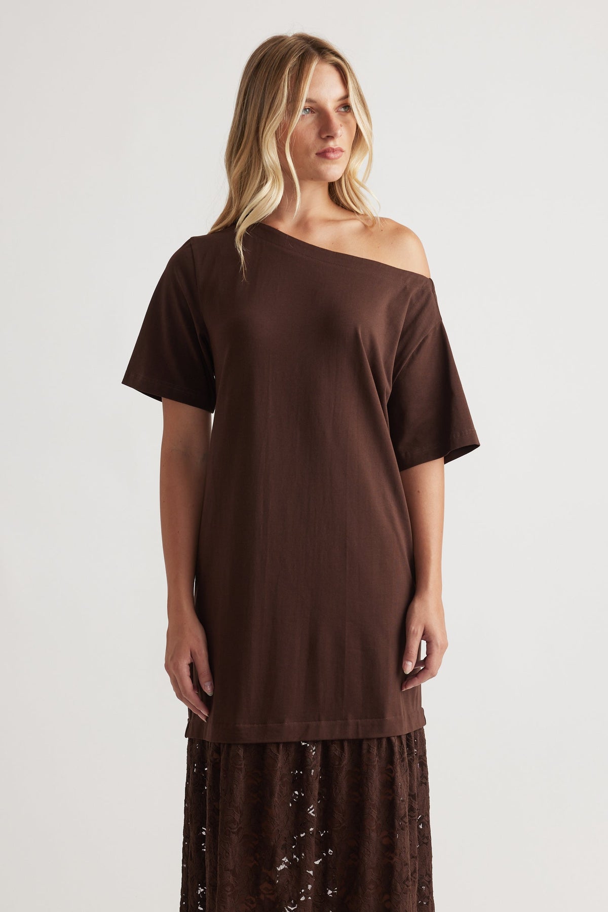Woman wearing Alexis Lace Maxi Dress in rich mocha with a relaxed off-shoulder top and intricate lace skirt by DECJUBA.