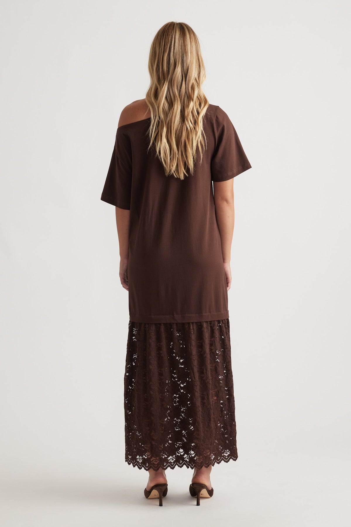 Woman wearing Alexis Lace Maxi Dress in rich mocha with relaxed fit top and intricate lace overlay skirt, paired with heels
