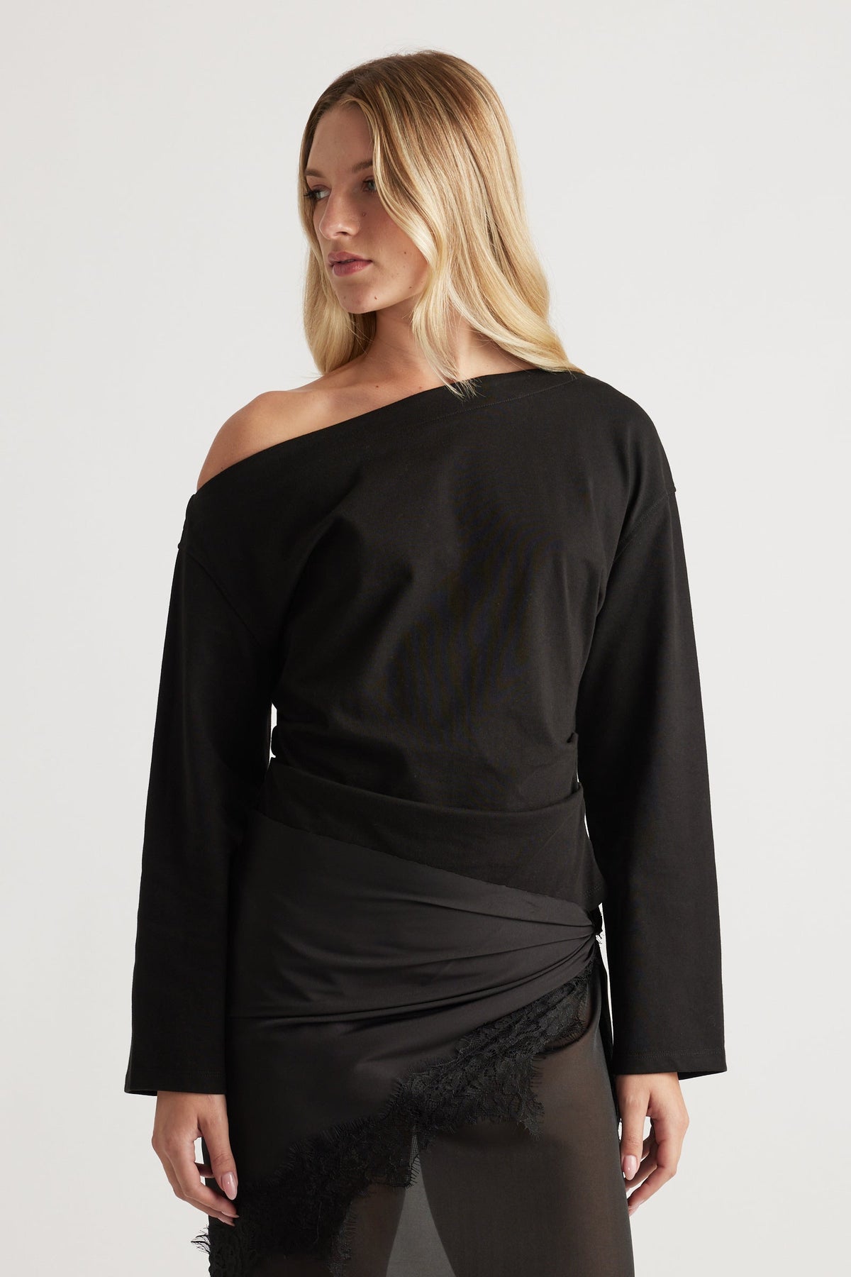 Woman wearing a black off-shoulder long sleeve top paired with a sheer lace-trimmed skirt for an elegant look