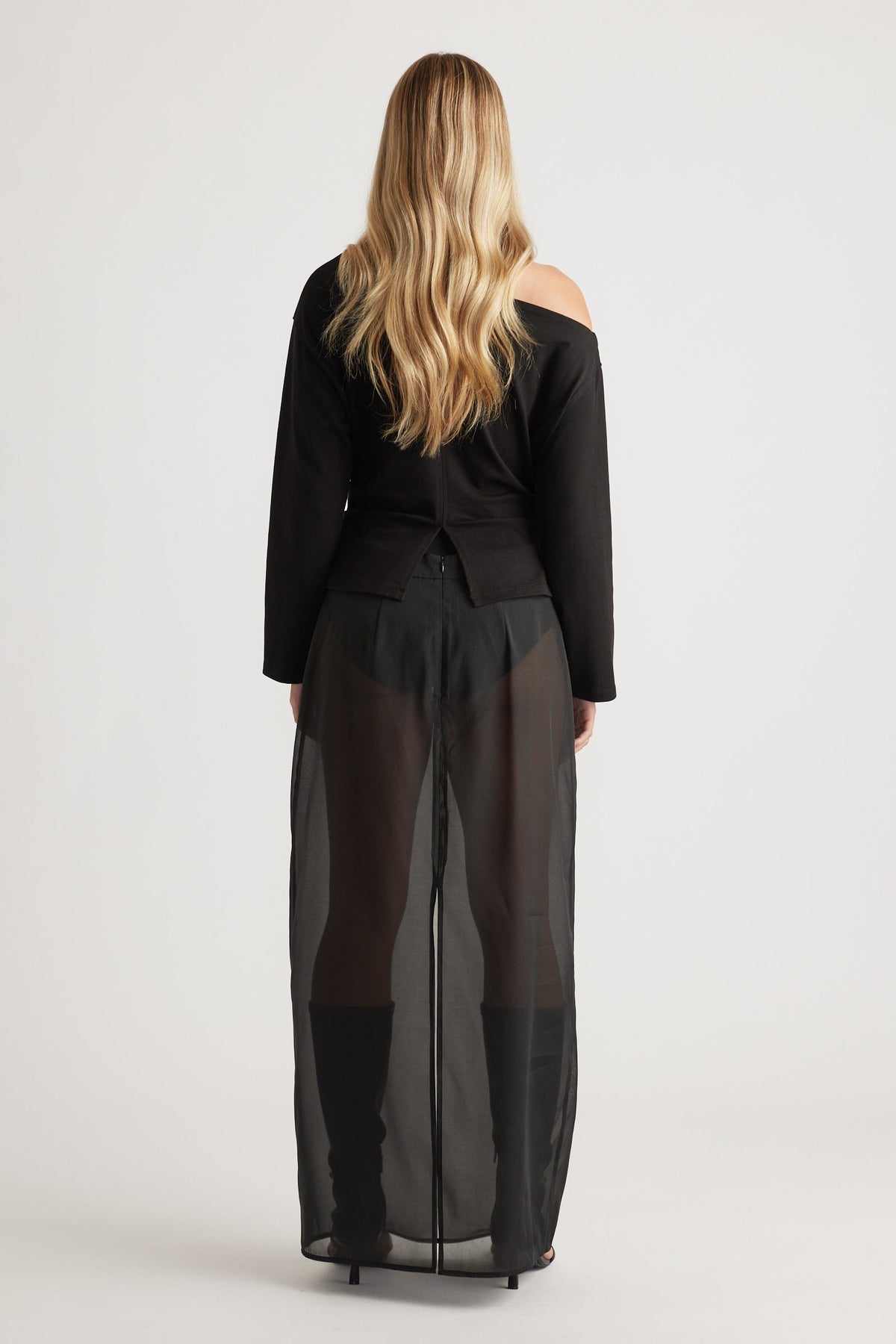 Woman wearing a black off-shoulder top paired with sheer wide-leg pants and knee-high black boots for a bold look