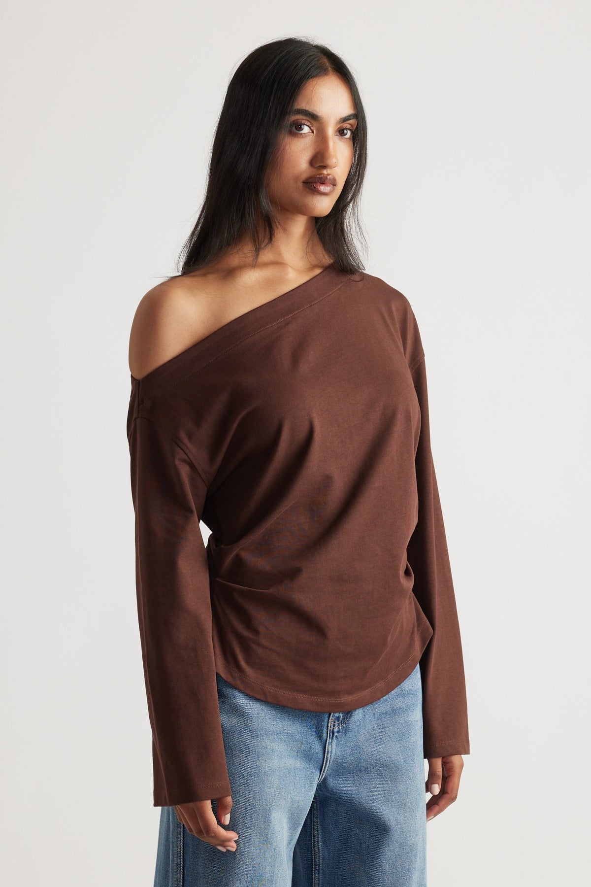 Woman wearing a relaxed-fit brown off-shoulder long sleeve tee paired with light blue wide-leg denim jeans.