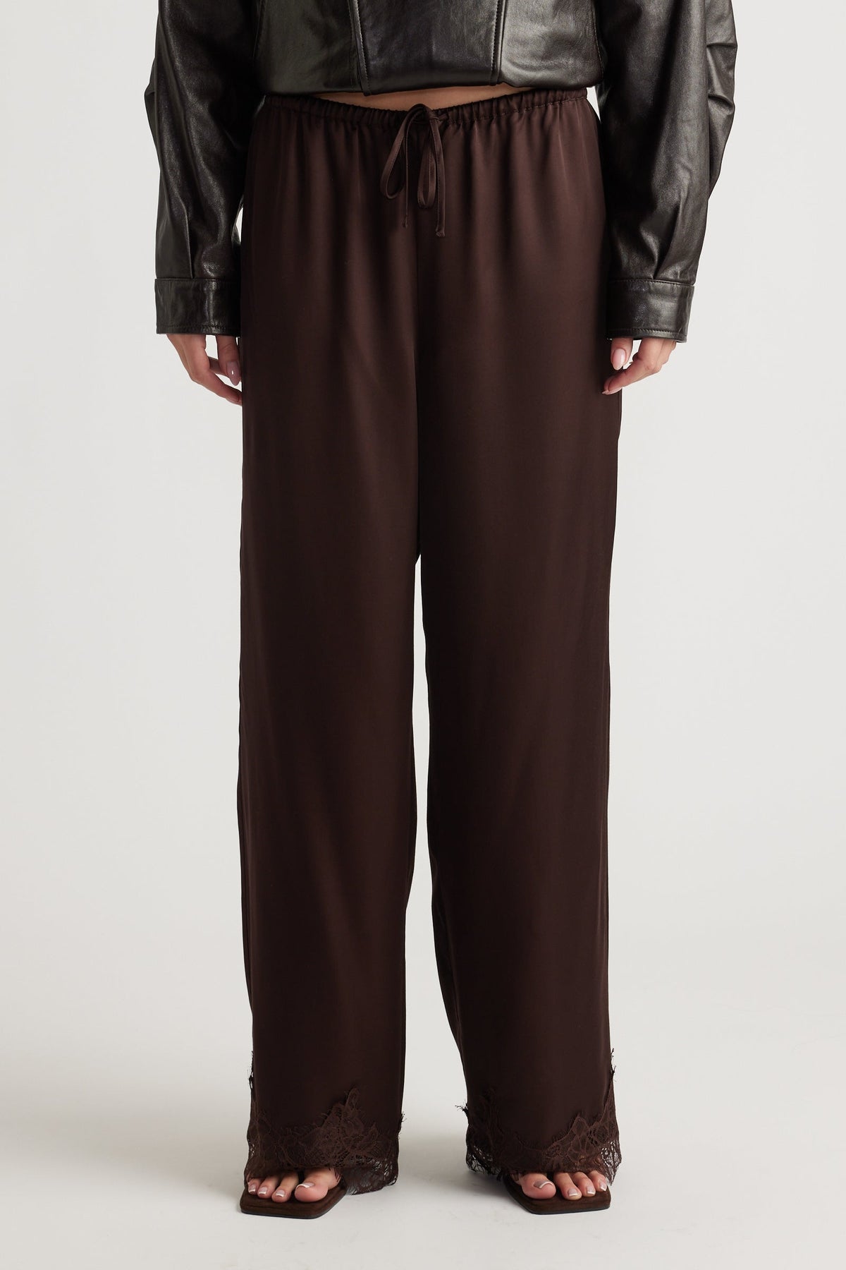 Dark brown satin pants with relaxed fit and delicate lace trim at the wide hems for a chic, comfortable look.