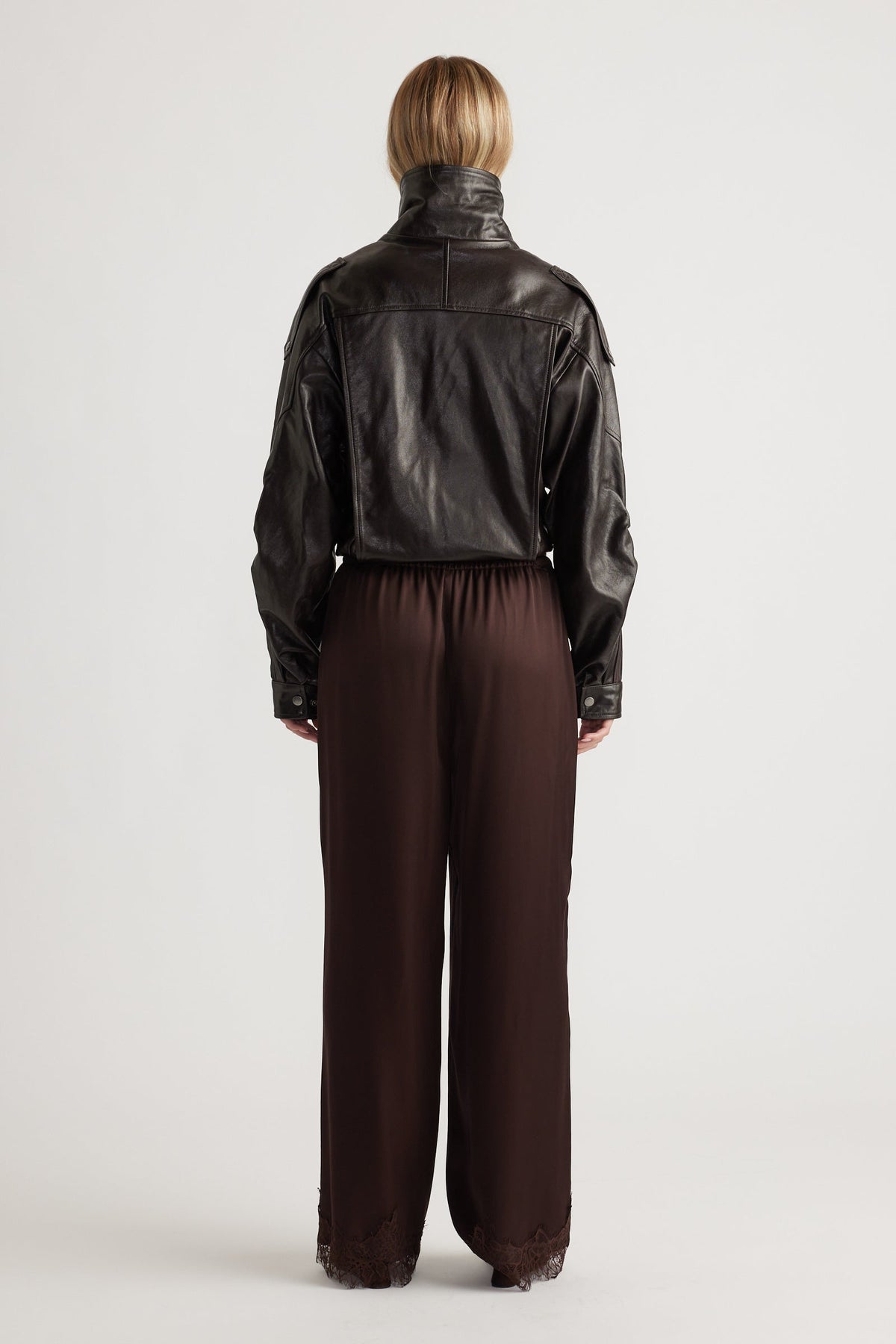 Back view of rich brown satin pants with lace trim at the hem, styled with a cropped black leather jacket