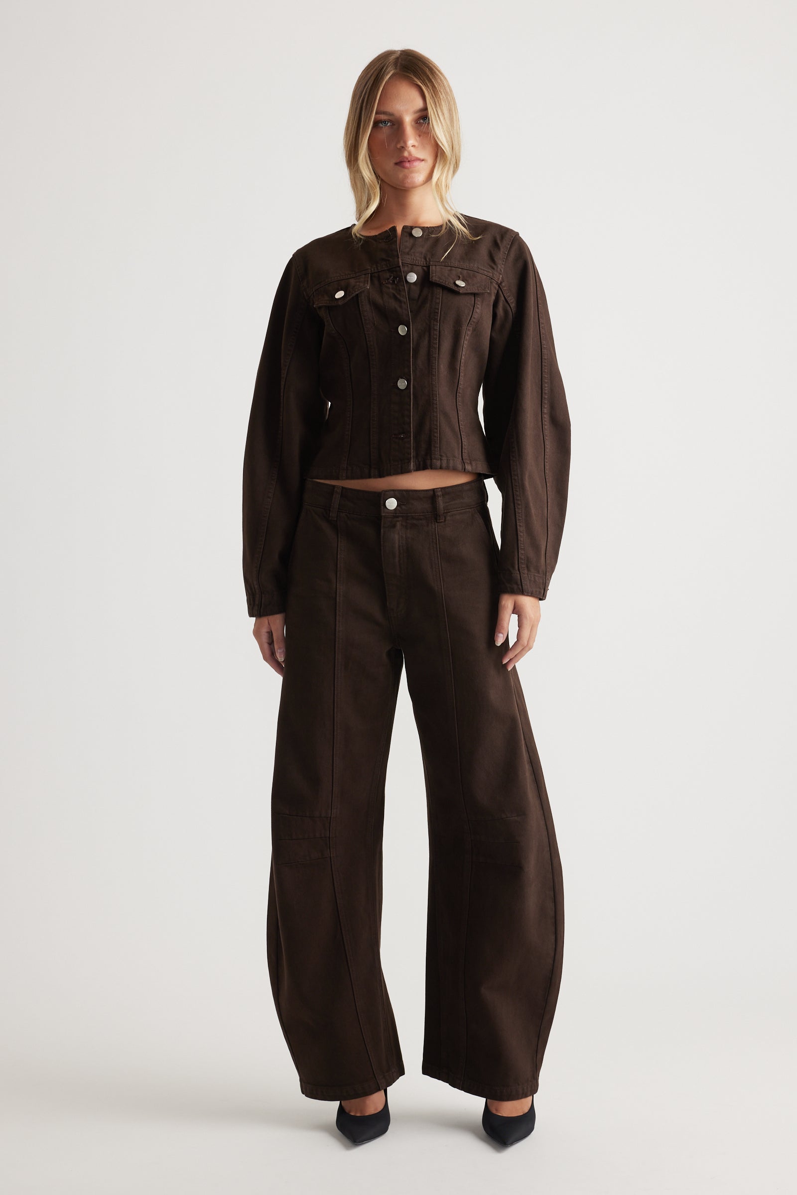 Woman wearing a brown denim jacket and barrel leg jeans on a white background