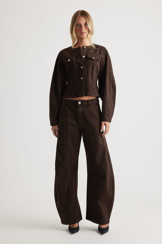 Woman wearing a brown denim jacket and barrel leg jeans on a white background