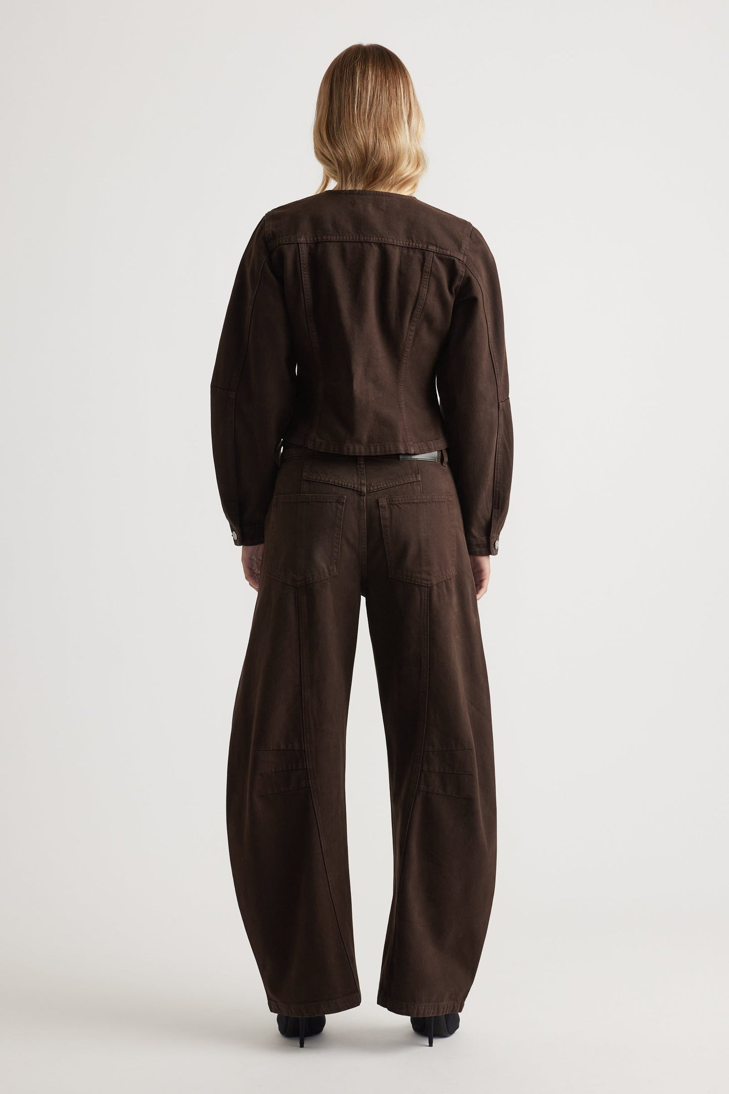 Person wearing a brown barrel leg jeans on a white background