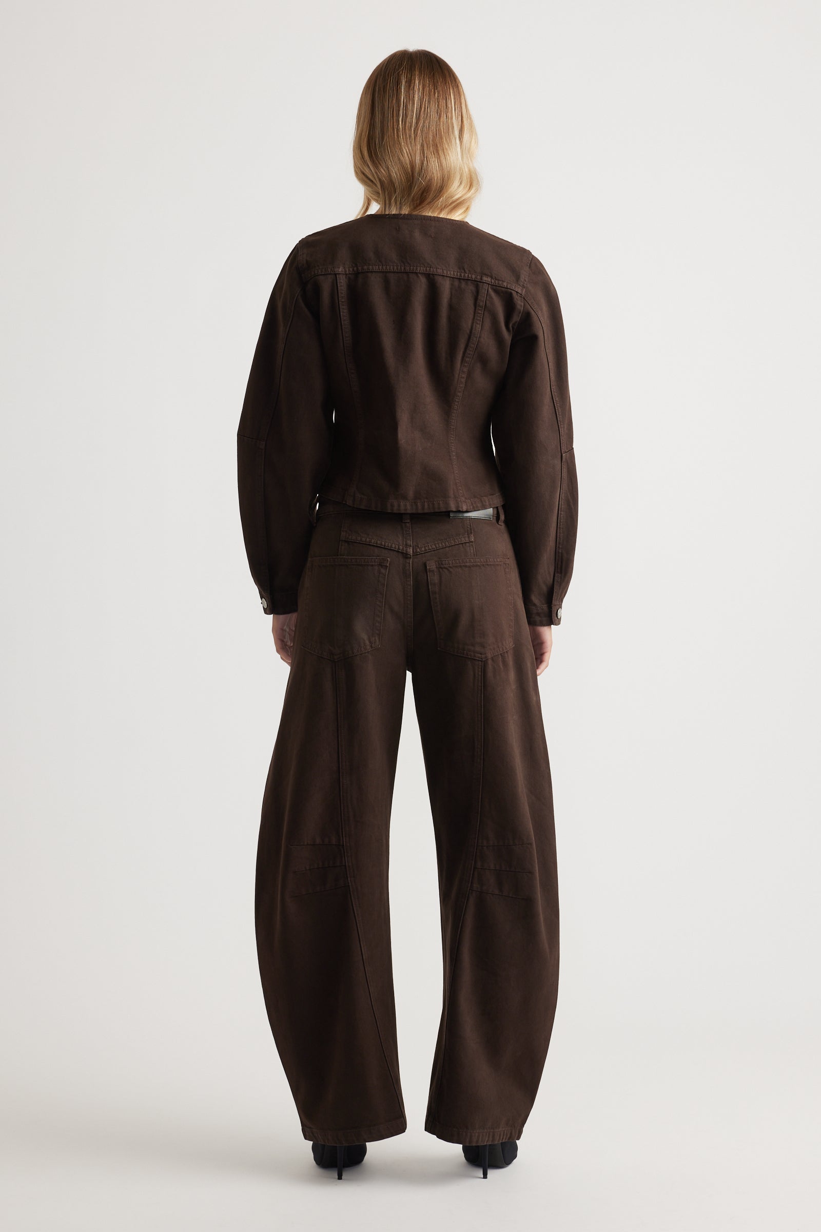 Person wearing a brown barrel leg jeans on a white background