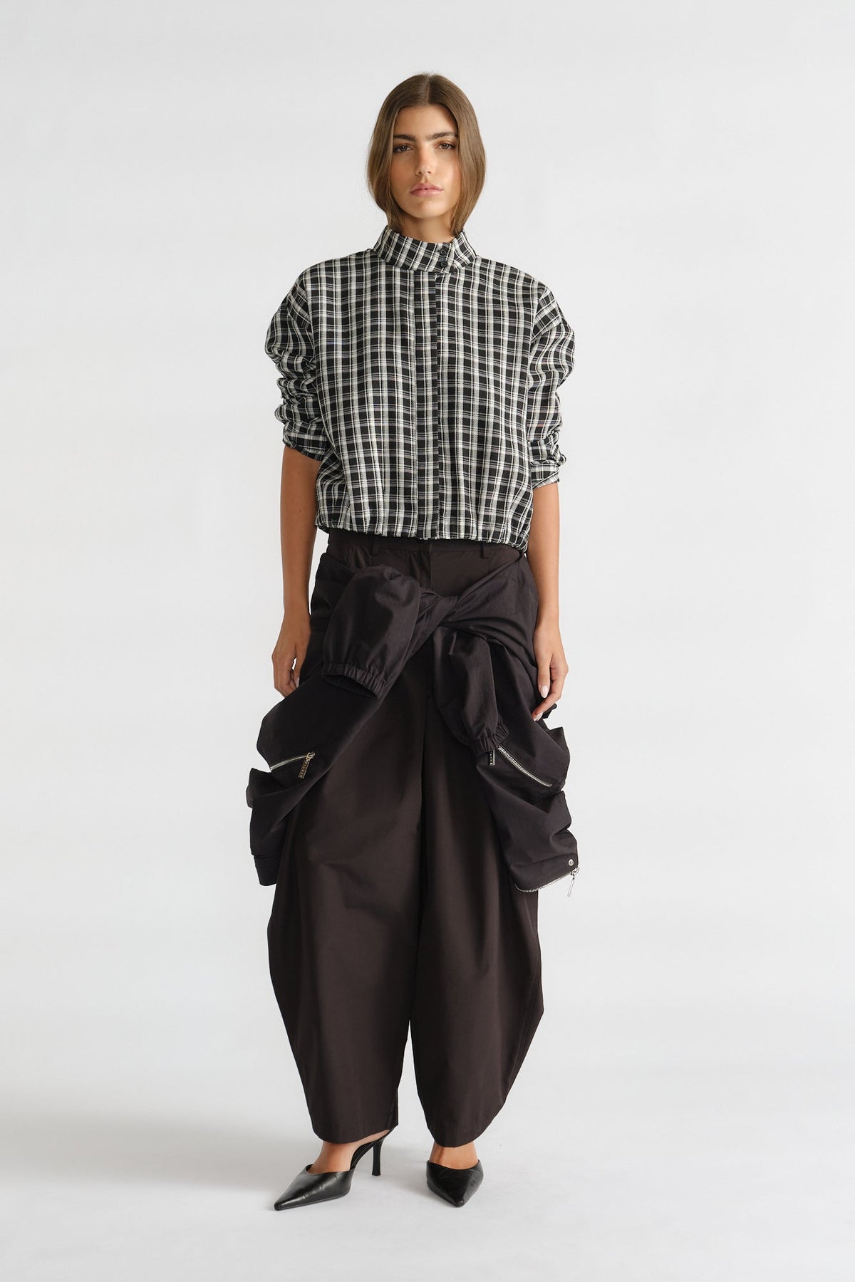 Woman wearing a relaxed-fit check shirt with ruched sleeves paired with wide-leg black pants and pointed heels