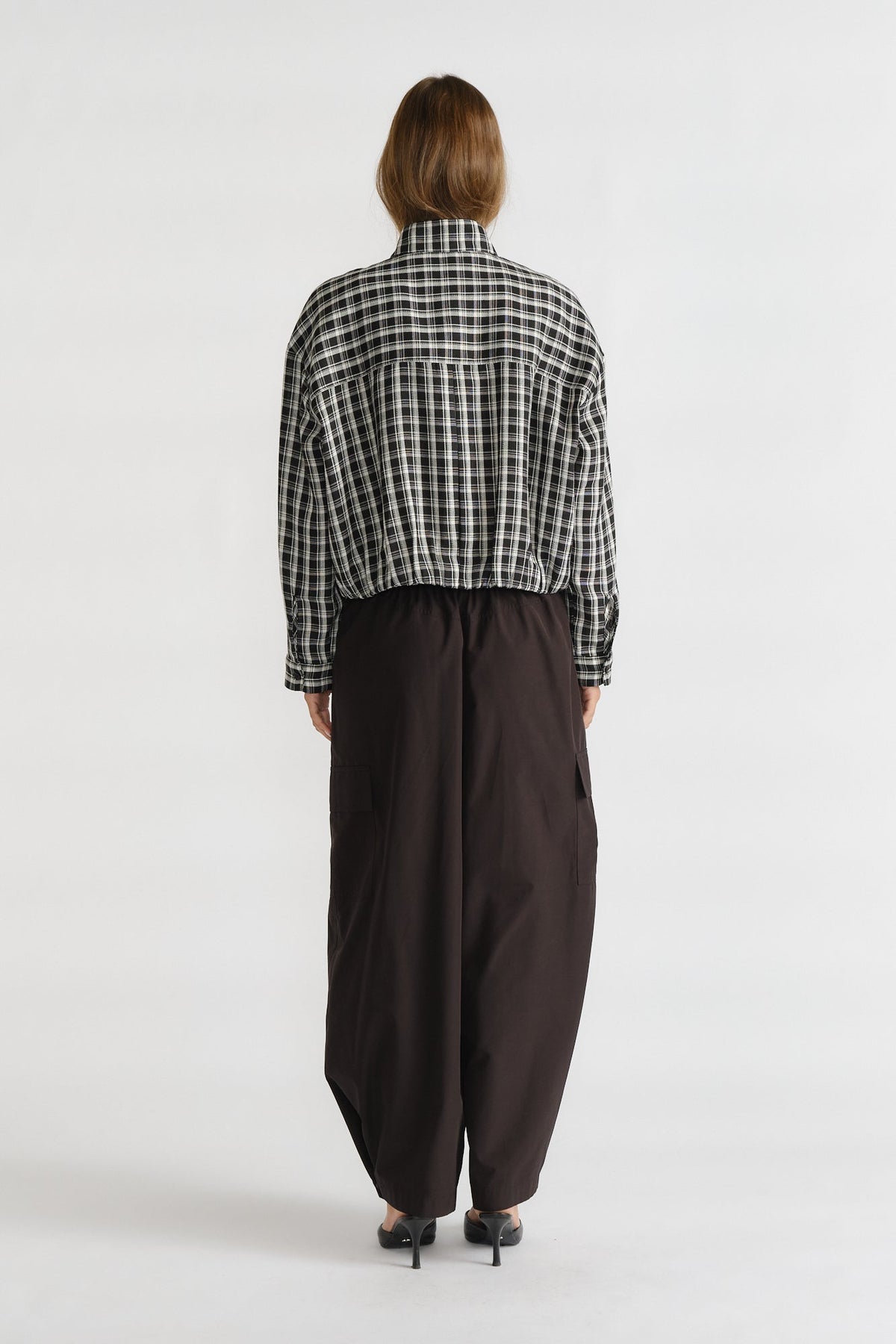 Woman seen from behind wearing a relaxed checkered boyfriend shirt paired with loose black wide-leg pants and heels.