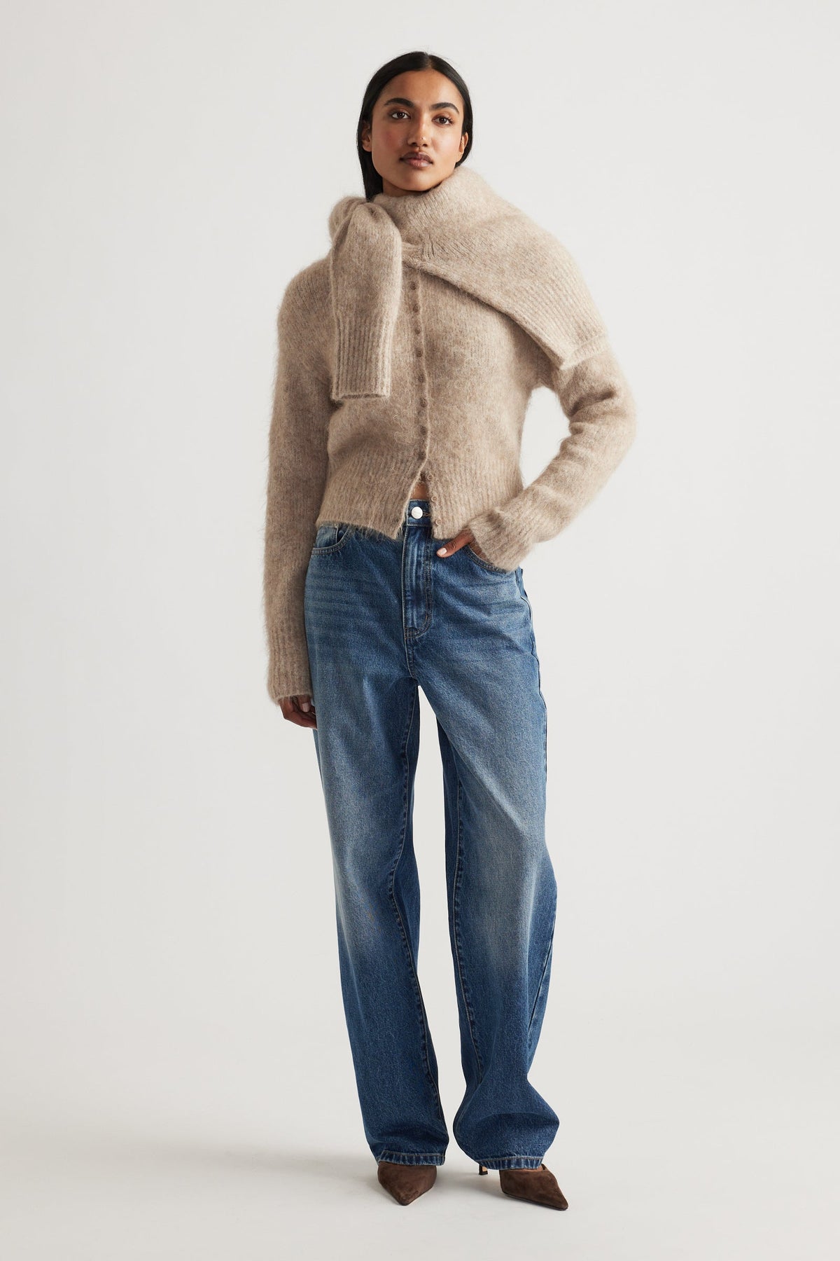 Woman wearing a soft beige alpaca blend cardigan layered with a matching scarf, paired with relaxed blue denim jeans.