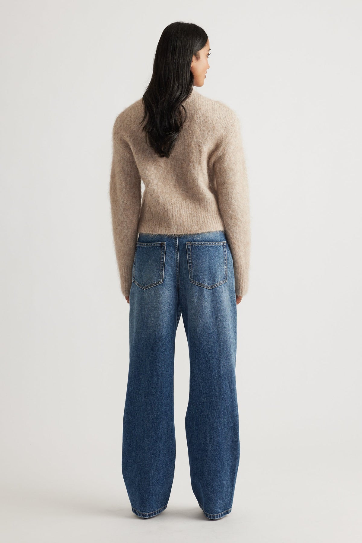 Rear view of woman wearing a soft beige alpaca blend cardigan paired with relaxed fit blue denim jeans