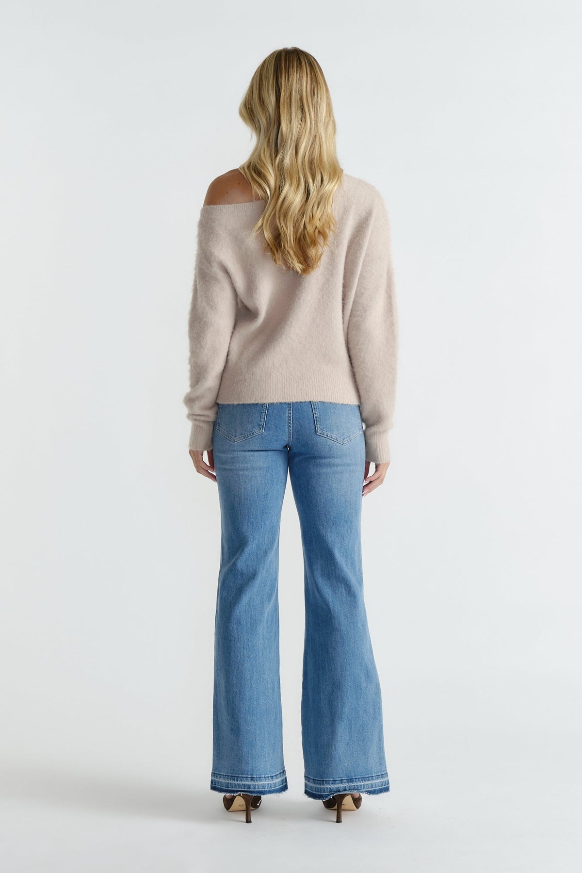 Rear view of woman wearing a soft beige off-shoulder knit paired with light-wash flared jeans and heels