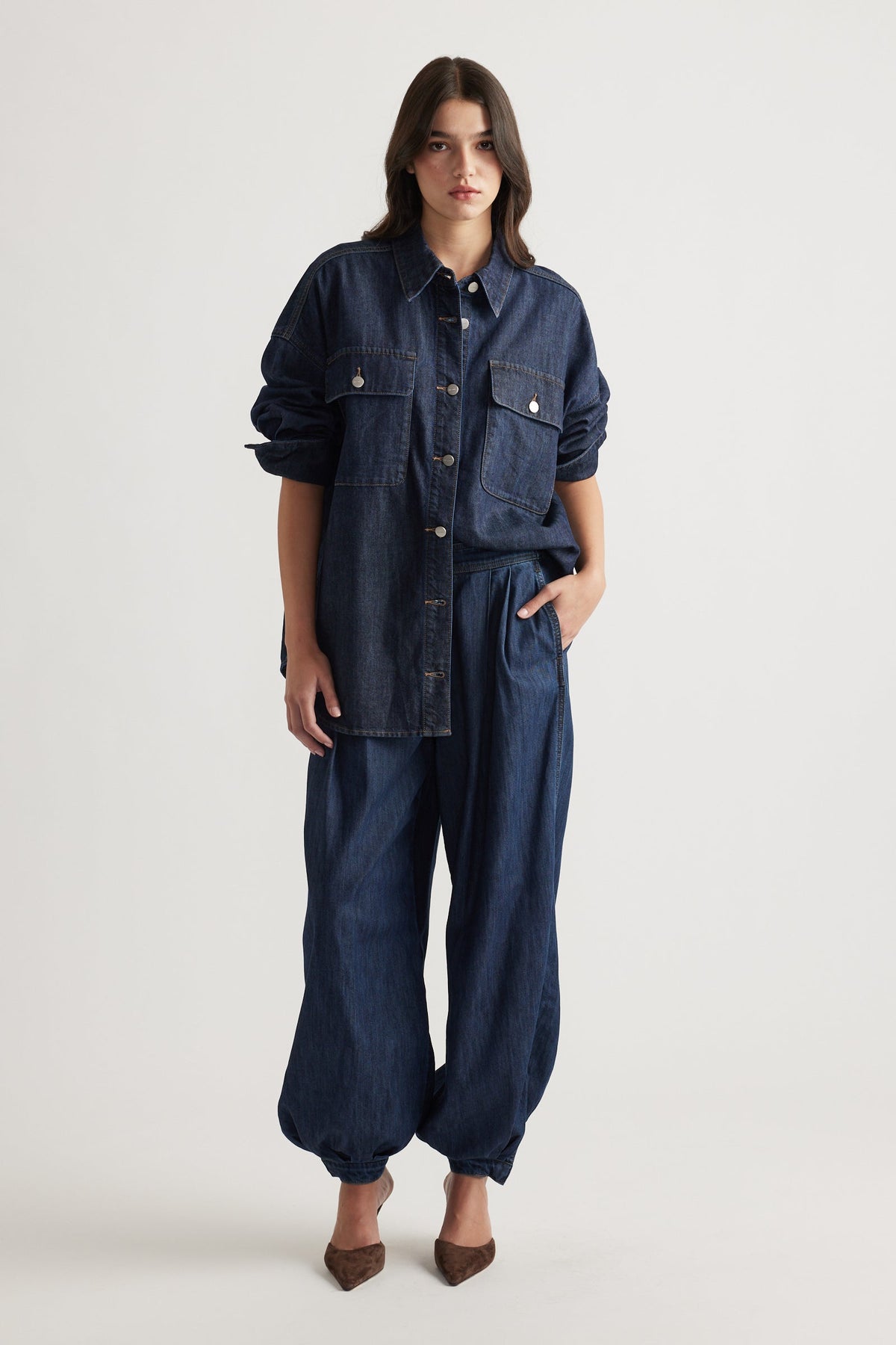 Woman wearing oversized dark denim shirt with large pockets and relaxed cuffed denim pants styled with brown heels