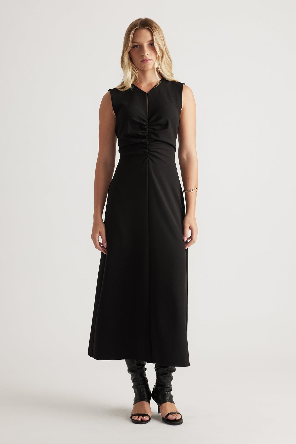 Sleeveless black midi dress with ruched front detail, flattering fitted waist and flowing skirt worn with heeled sandals.