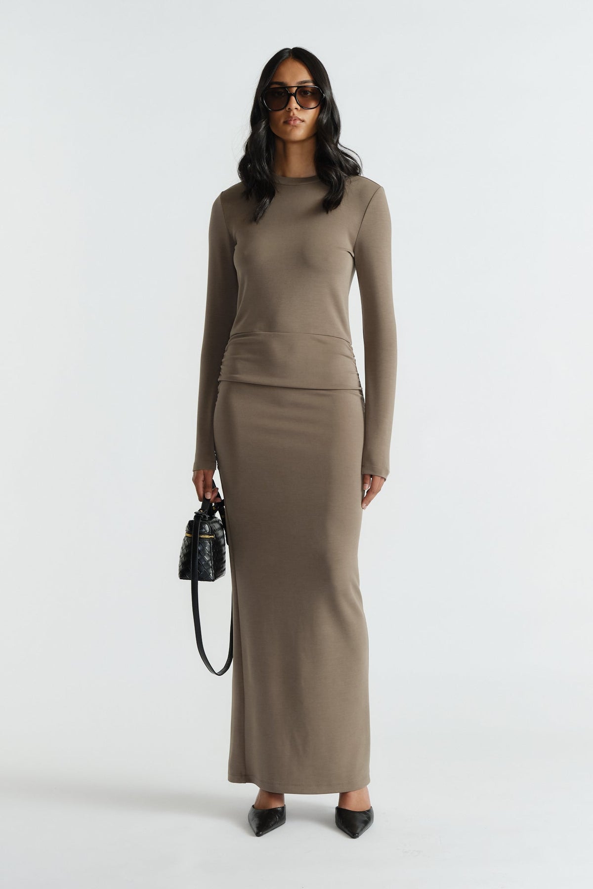 Woman wearing a sleek khaki long-sleeve midi dress with a fitted silhouette, accessorized with black bag and heels